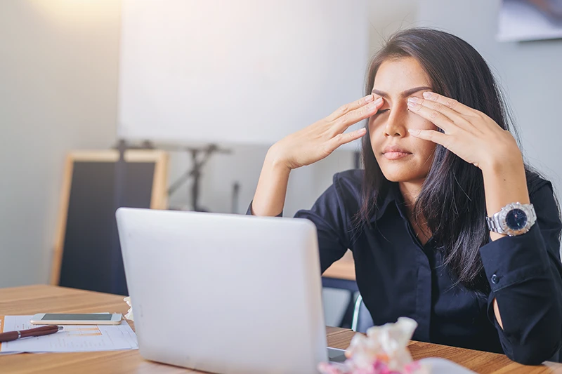 a woman working on her laptop and rubbing her eyes