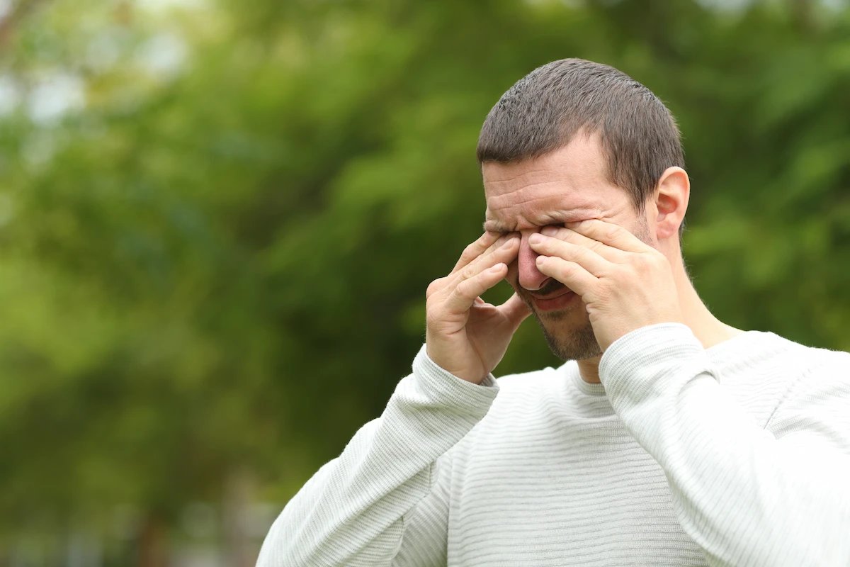 burning_eyes man rubbing his irritated eyes outdoors