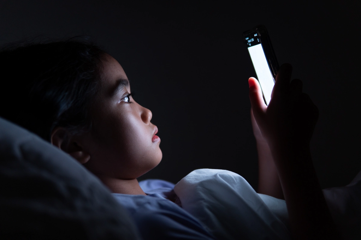screen-time-myopia Child lying in bed using a smartphone at night